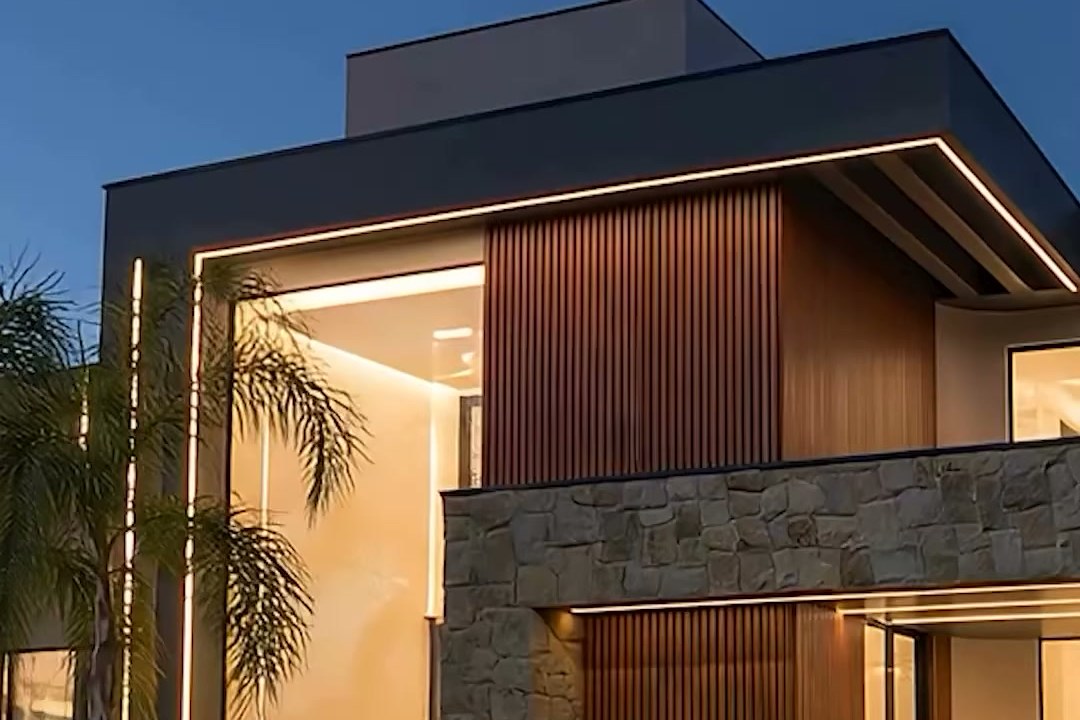 Fachada da Casa Tango ao entardecer: pedra, madeira ripada e iluminação linear